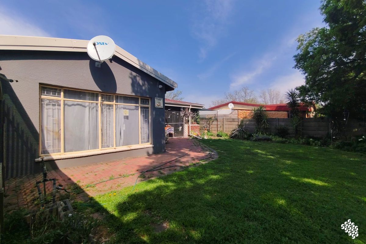 Rear view of the property featuring a brick paved patio area, a well-maintained lawn, and secure boundary walling.