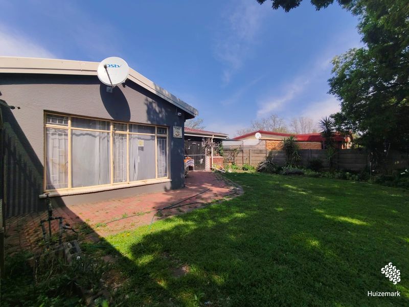 Rear view of the property featuring a brick paved patio area, a well-maintained lawn, and secure boundary walling.