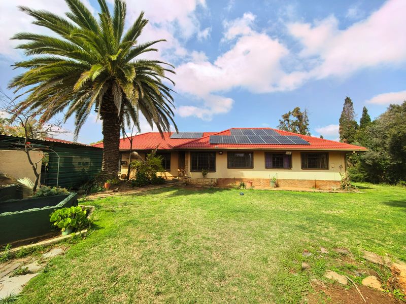 Rear view of the house featuring a red tiled roof with installed solar panels, brick exterior walls, and a spacious garden area.