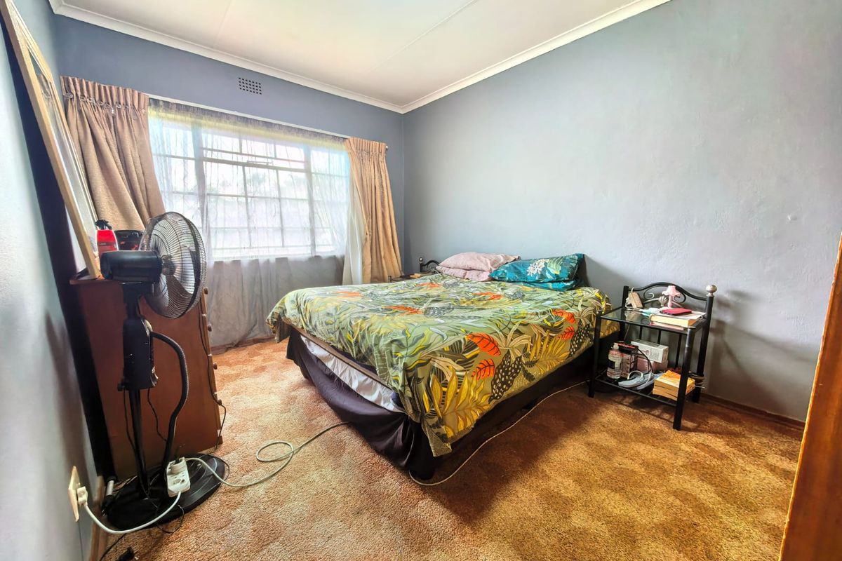 A bedroom featuring a large window, coved ceilings, and carpet flooring, offering a functional space with potential for cosmetic updates.