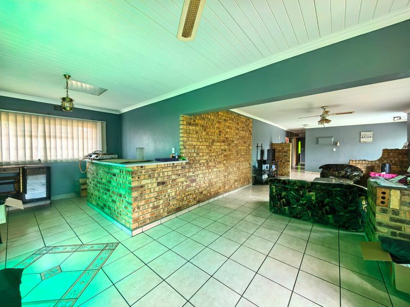 Spacious open-plan living area featuring a built-in brick bar, exposed brick feature wall, ceramic tile flooring, and a tongue and groove ceiling.