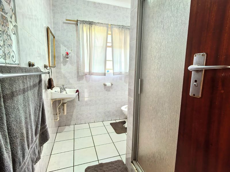 A functional bathroom featuring a shower enclosure, wall-mounted basin, and tiled finishes, offering a practical layout with potential for modern updates.