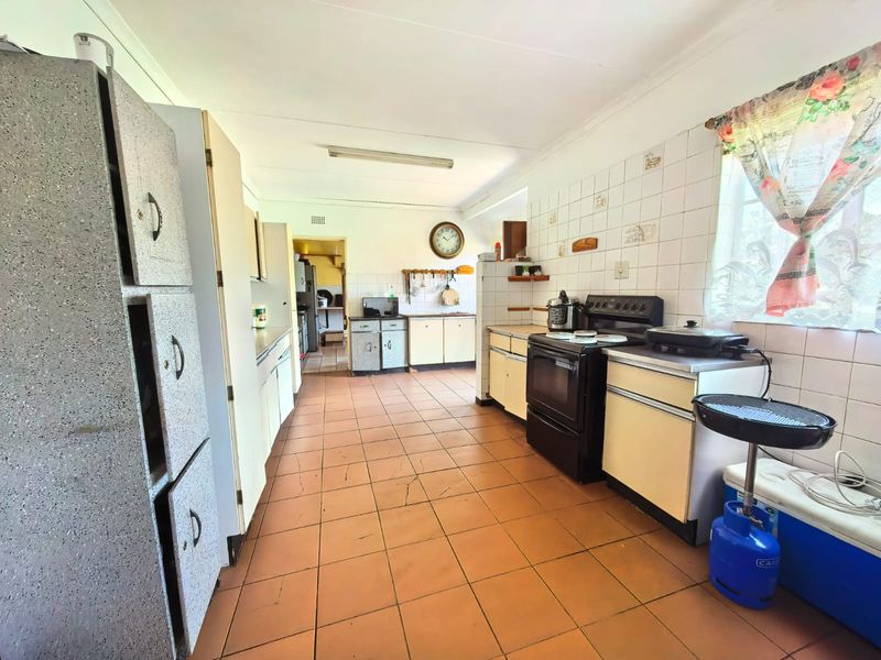 A spacious, dated kitchen featuring tiled flooring, extensive cabinetry, and a freestanding oven, offering significant potential for a modern renovation.