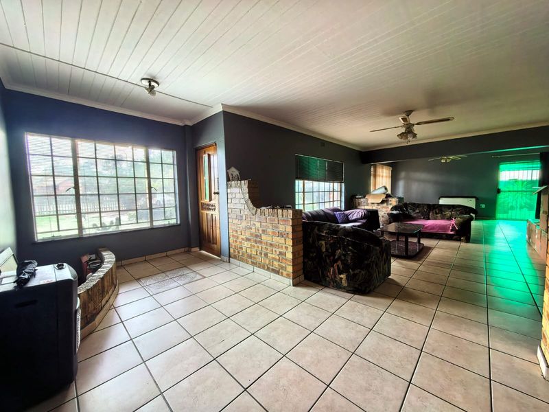 Spacious open-plan living area featuring tiled flooring, an exposed brick partition wall, and ceiling fans, offering a versatile layout for family living.