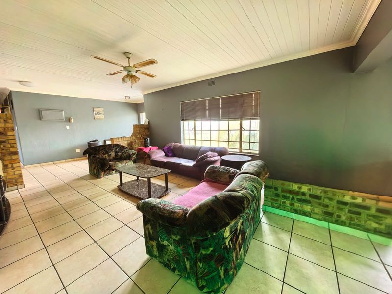 Spacious living room featuring tiled flooring, a timber panelled ceiling, ceiling fan, and an exposed brick feature wall with integrated lighting.