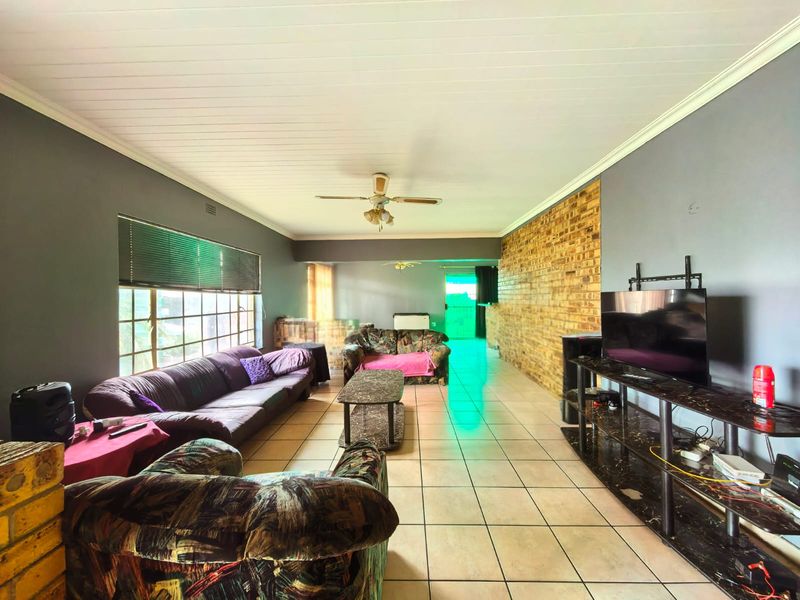 Spacious living room featuring a prominent exposed brick wall, tiled flooring, and a ceiling fan, offering a versatile layout for relaxation.