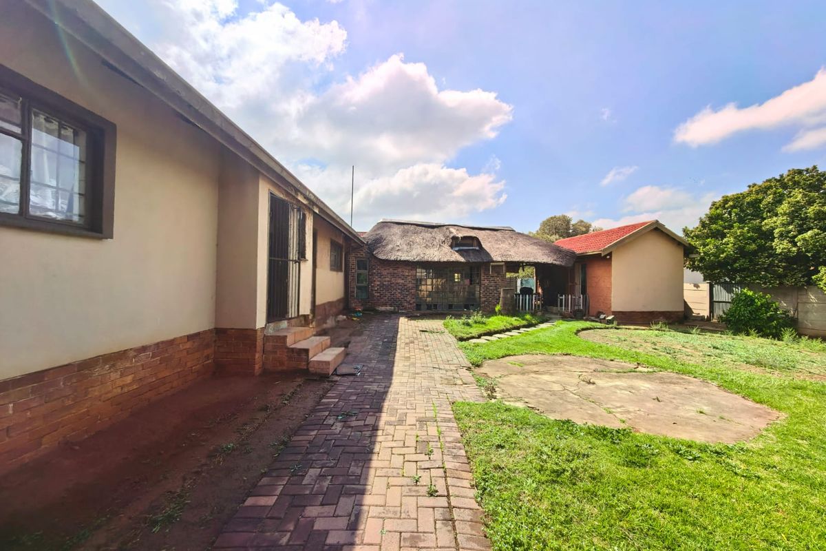 Rear view of the property featuring a brick paved walkway, a combination of thatched and tiled roofing, and an expansive garden area.