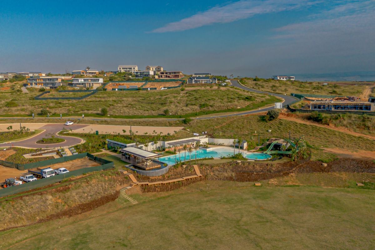 Aerial view of a residential estate featuring a communal swimming pool, water slide, clubhouse, and surrounding landscaped grounds within a developing neighborhood.