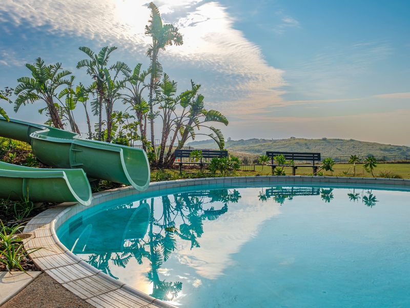 A well-maintained outdoor swimming pool featuring a built-in water slide, surrounded by landscaped greenery and scenic hillside views.