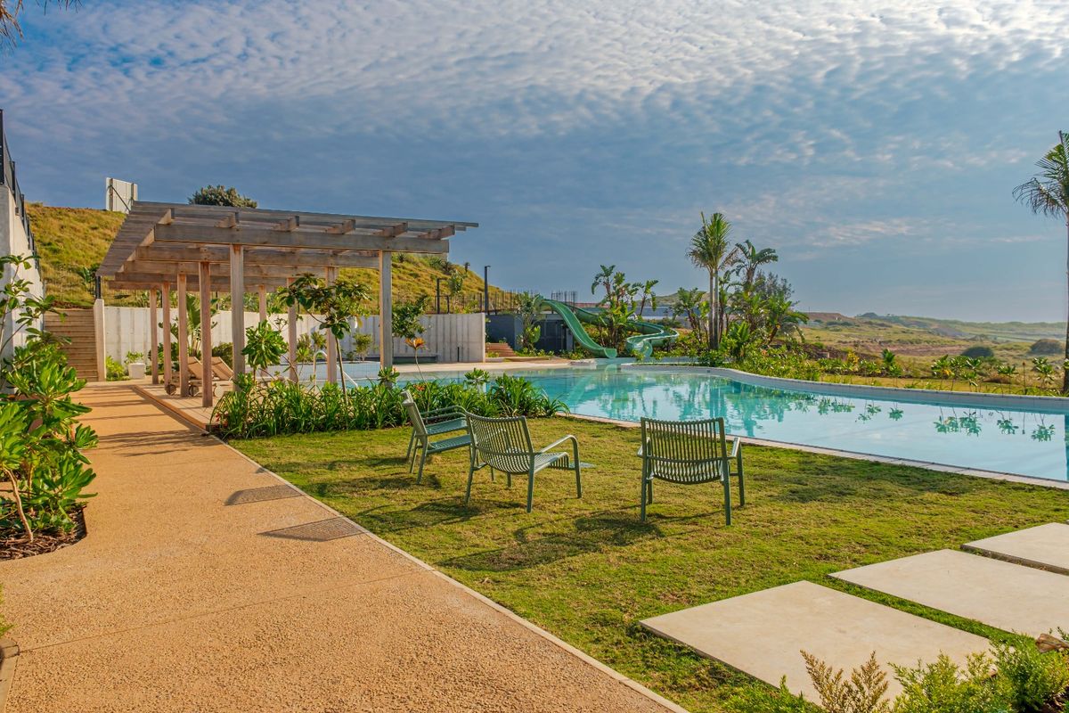 A well-maintained outdoor pool area featuring a swimming pool, water slide, wooden pergola, and landscaped garden with scenic views.