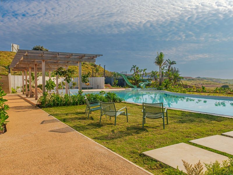 A well-maintained outdoor pool area featuring a swimming pool, water slide, wooden pergola, and landscaped garden with scenic views.