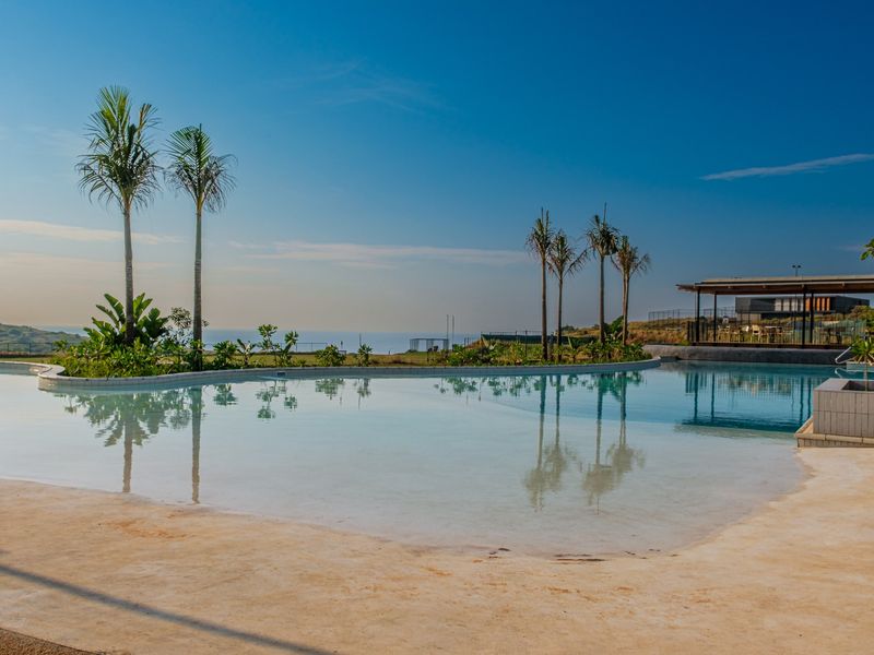 A well-maintained swimming pool area featuring a beach-entry design, landscaped surroundings, and scenic coastal views.