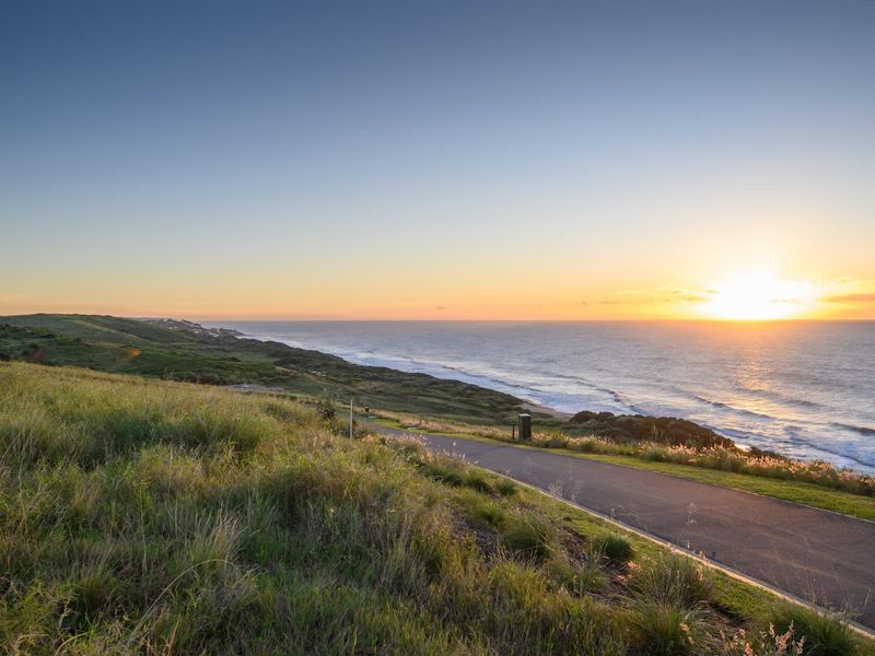 A scenic view of the coastline and ocean at sunset, featuring a paved road winding through the natural landscape.
