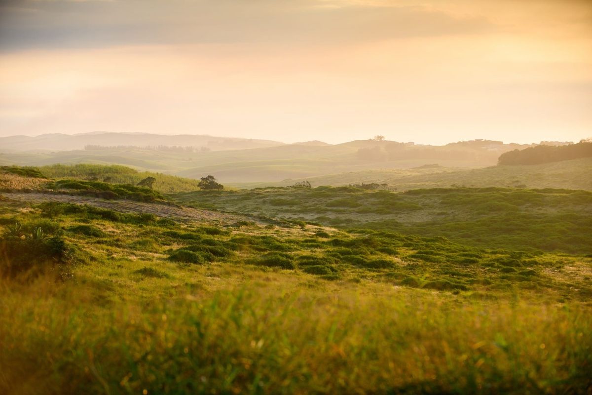 A scenic, elevated view of rolling green hills and natural landscape at sunset, showcasing the property's expansive outdoor surroundings.