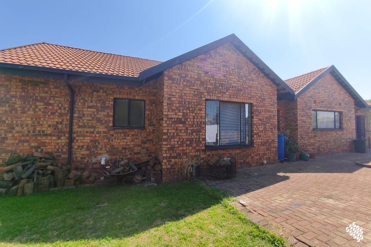 Rear view of a face brick house featuring a tiled roof, paved patio area, and aluminium window frames.