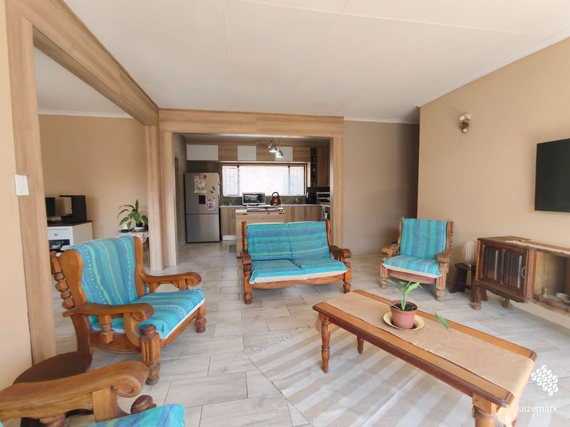 Open-plan living area featuring tiled floors and timber-look structural framing, seamlessly connecting to a functional kitchen space.
