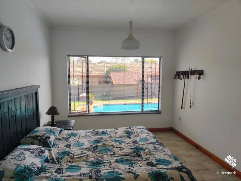 A bedroom featuring tiled flooring, a pendant light, and a window with security bars overlooking the swimming pool area.