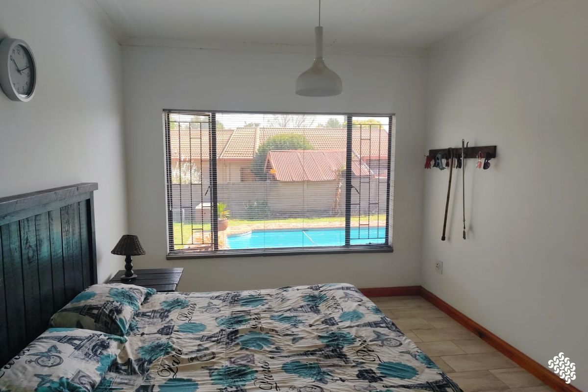 A bedroom featuring tiled flooring, a pendant light, and a window with security bars overlooking the swimming pool area.