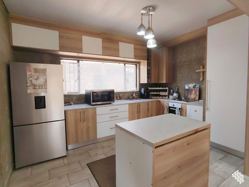 A functional kitchen featuring modern wood-tone and white cabinetry, tiled flooring, and a central island, with some wall finishes requiring completion.