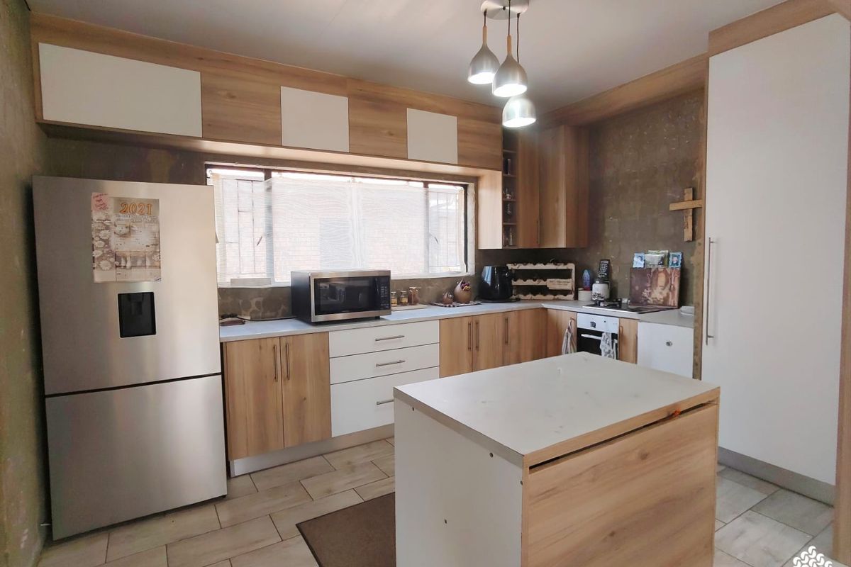 A functional kitchen featuring modern wood-tone and white cabinetry, tiled flooring, and a central island, with some wall finishes requiring completion.