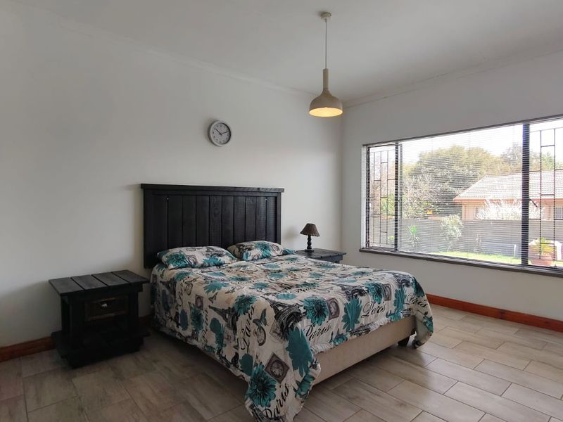 A spacious bedroom featuring neutral tiled flooring, a large window with security bars, and a central pendant light fixture.