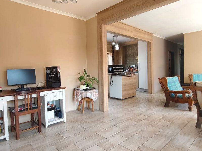 Spacious open-plan living area featuring neutral tiled flooring, a decorative timber-look beam, and a seamless transition into the adjoining kitchen space.