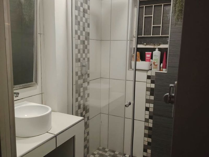 A modern bathroom featuring a glass shower enclosure with a rain shower head, a vessel sink vanity, and decorative mosaic tile accents.