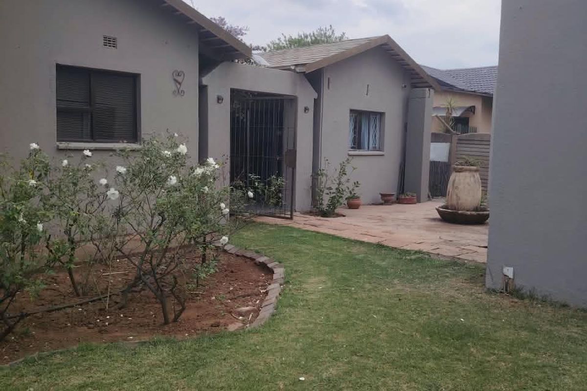 A view of the rear exterior of the house featuring a paved patio area, lawn, and secure gated entrance.