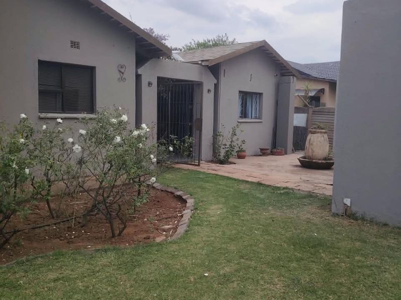 A view of the rear exterior of the house featuring a paved patio area, lawn, and secure gated entrance.