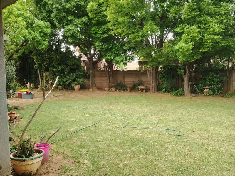 A spacious rear garden featuring a concrete patio area, established mature trees, and a secure precast concrete boundary wall.