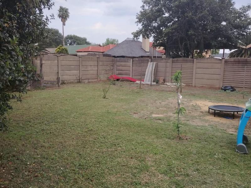 A spacious backyard featuring a lawn area enclosed by a precast concrete boundary wall.