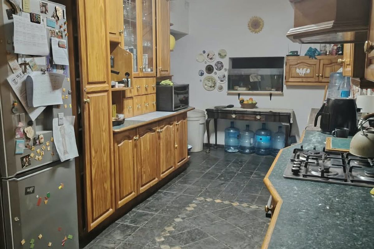 A functional kitchen featuring traditional wooden cabinetry, a gas hob with extractor hood, and dark tiled flooring, offering potential for a modern update.