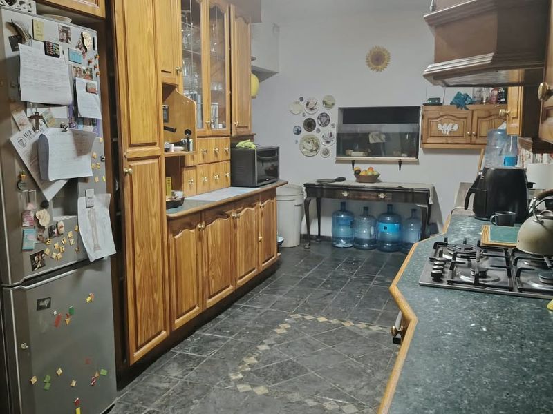 A functional kitchen featuring traditional wooden cabinetry, a gas hob with extractor hood, and dark tiled flooring, offering potential for a modern update.