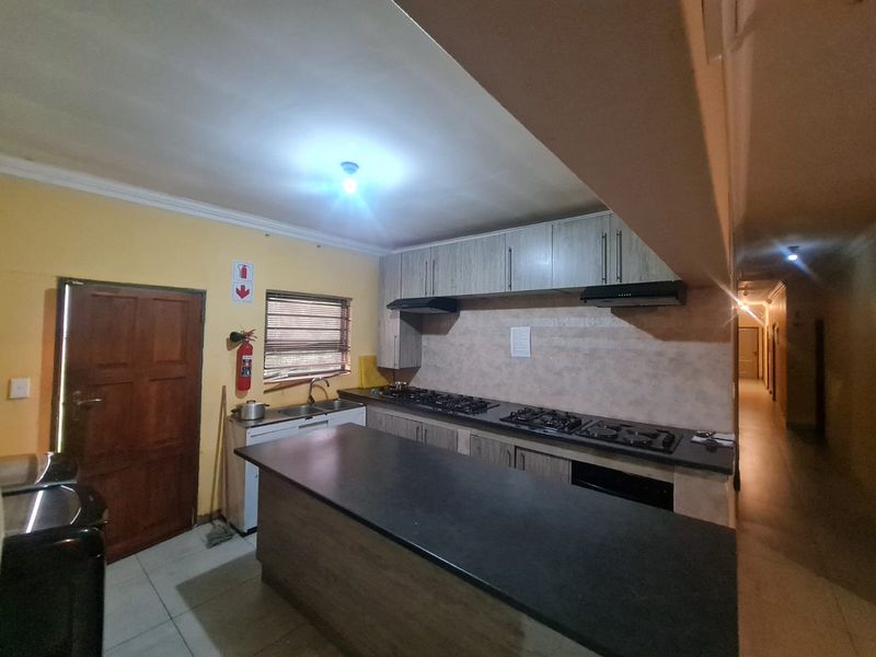 Kitchen featuring built-in cabinetry, double gas hobs with extractor fans, a central island, and tiled flooring, leading into a hallway.