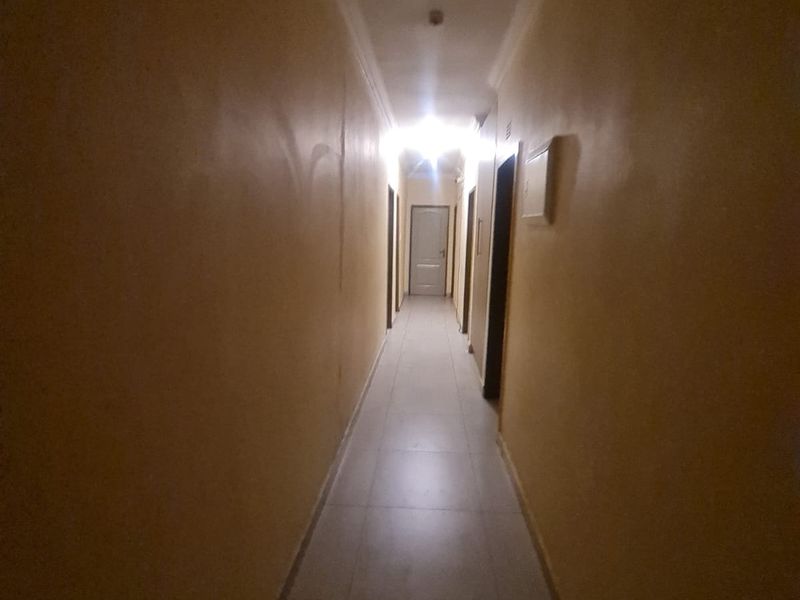 A long, narrow interior hallway featuring tiled flooring and multiple internal doors, currently empty and requiring cosmetic updates.