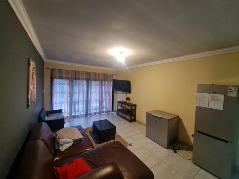 A living room featuring tiled flooring, cove cornicing, and a sliding glass door with security gate access to the exterior.