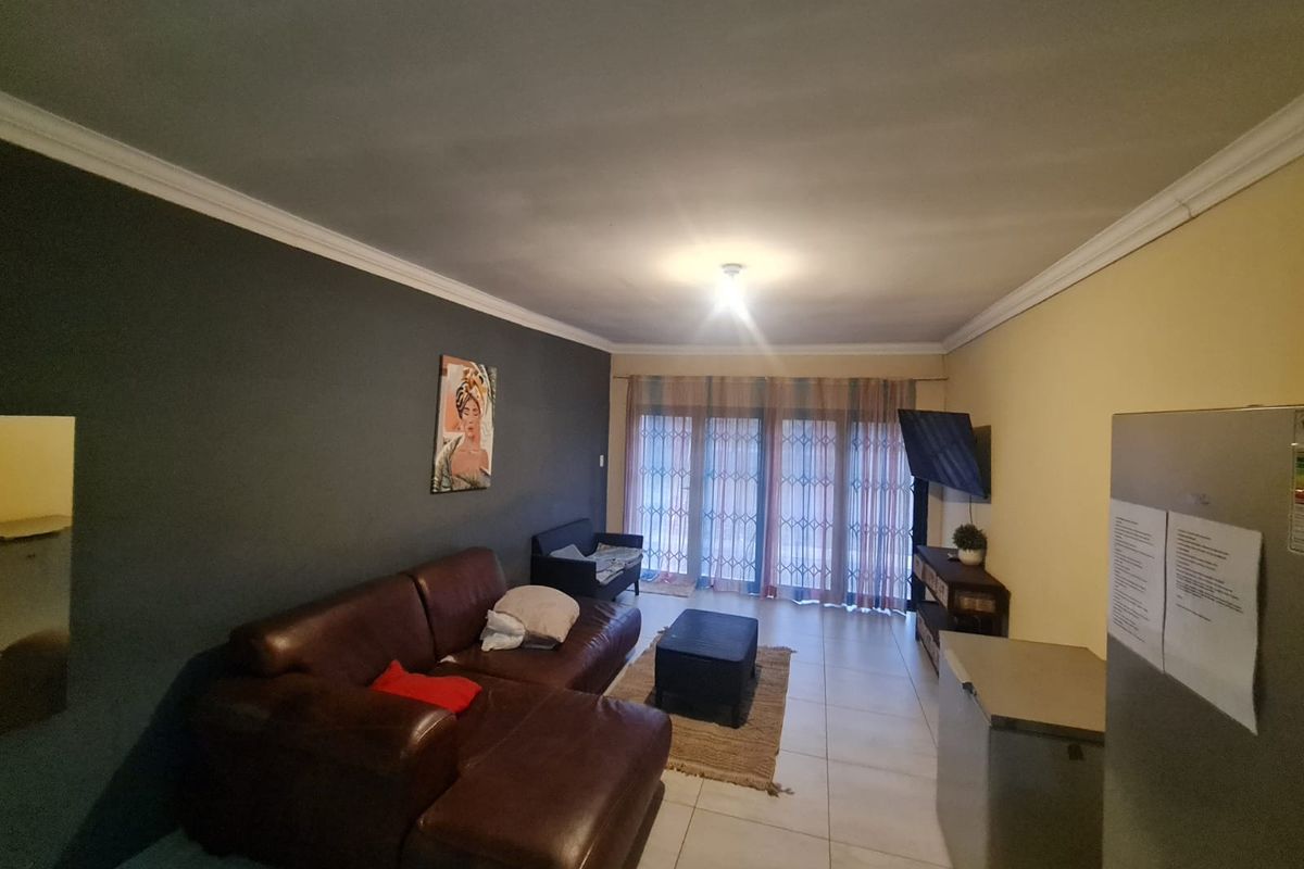 A living room featuring tiled flooring, ceiling cornicing, and sliding glass doors with security gates leading to the exterior.