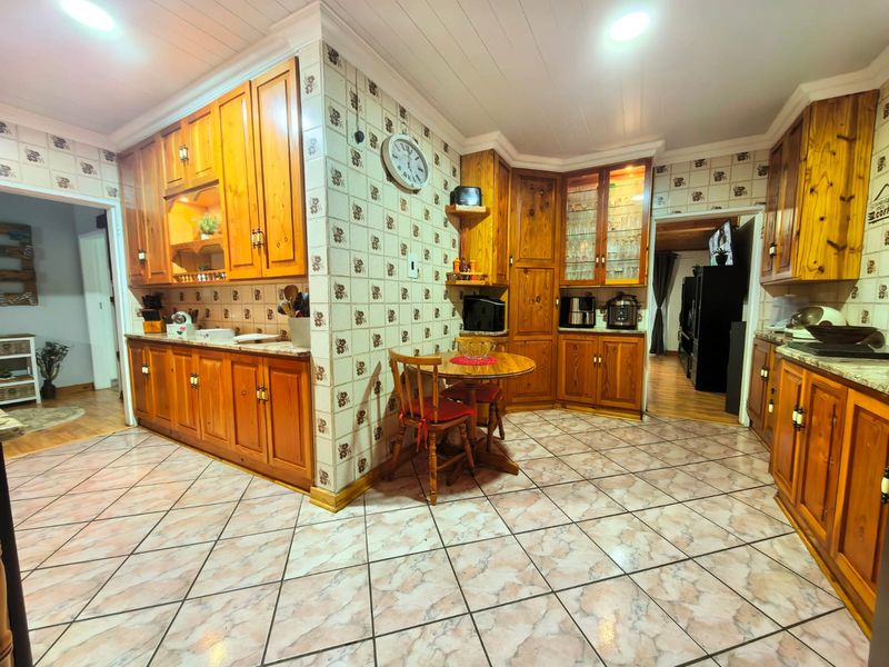 A spacious kitchen featuring extensive wooden cabinetry, patterned tiled backsplash, and tiled flooring, offering a traditional aesthetic with ample storage and display space.