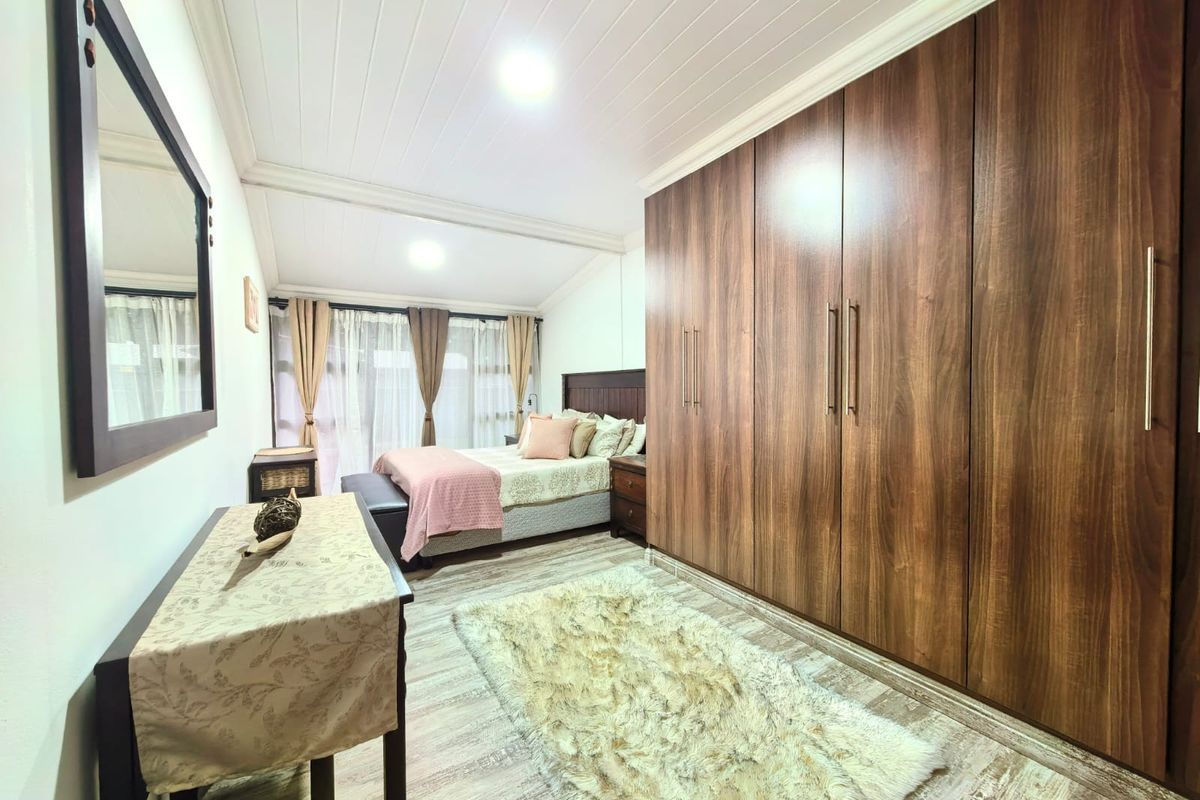 Spacious bedroom featuring extensive built-in wooden cupboards, modern laminate flooring, and a high-pitched tongue and groove ceiling with recessed lighting.