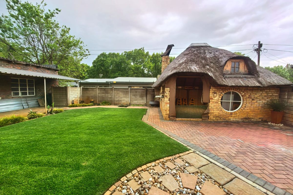 A well-maintained rear garden featuring a unique thatched-roof structure with a brick facade, paved patio area, and a neat lawn.