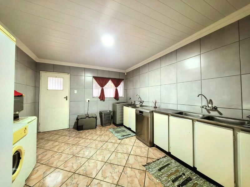A functional laundry room featuring tiled walls, tiled flooring, built-in cabinetry, and a double stainless steel sink.
