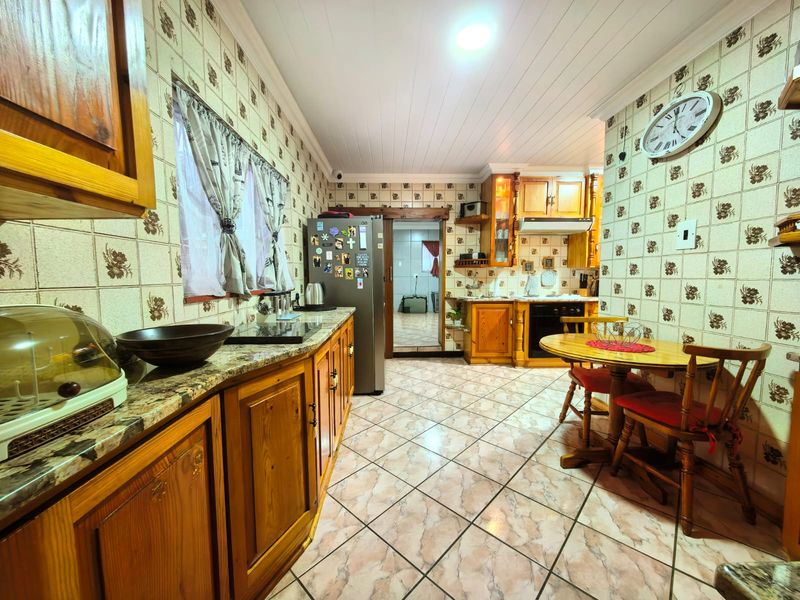 A traditional kitchen featuring wooden cabinetry, granite countertops, built-in oven, extractor fan, and patterned wall tiles with tiled flooring.