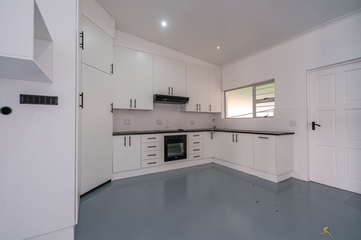 A clean, modern kitchen featuring white cabinetry, a built-in oven, extractor fan, and durable grey epoxy flooring.