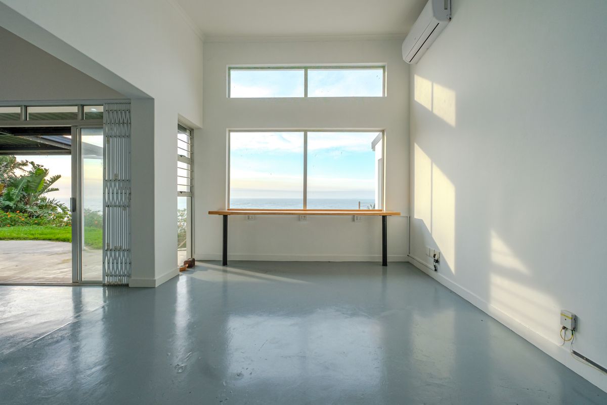Bright and airy living space featuring a built-in desk, split-system air conditioning, and large windows offering expansive ocean views with direct patio access.
