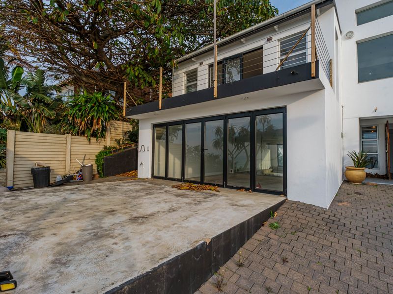Rear exterior view featuring a paved patio, concrete slab, and a balcony with steel railings, accessible via large black-framed bi-fold doors.