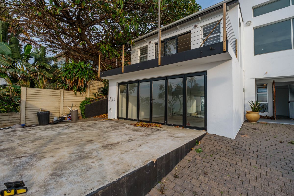 Rear exterior view featuring a paved patio, concrete slab, and a balcony with steel railings, accessible via large black-framed bi-fold doors.