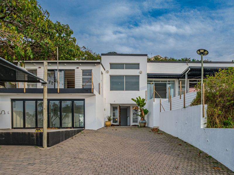 Front elevation of a modern multi-level home featuring a paved driveway, balcony access, and large glass sliding doors.