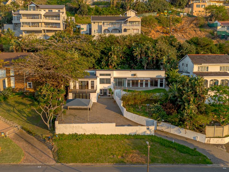 Aerial view of a multi-level residential property featuring a paved driveway, retaining walls, and balcony access, situated in a coastal hillside neighborhood.
