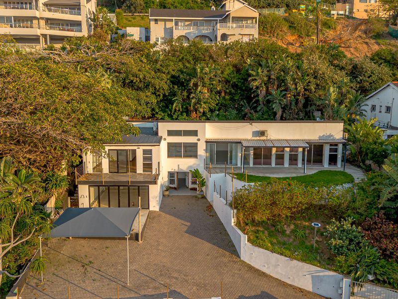 Aerial view of a multi-level residential property featuring a paved driveway, covered patio, balcony, and terraced garden areas.