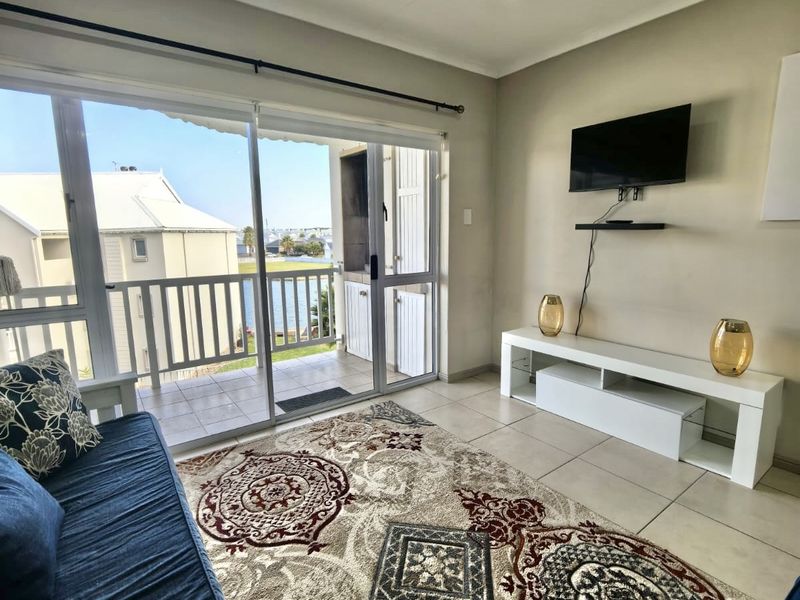 A bright living room featuring large sliding glass doors that open onto a balcony with water views and tiled flooring throughout.